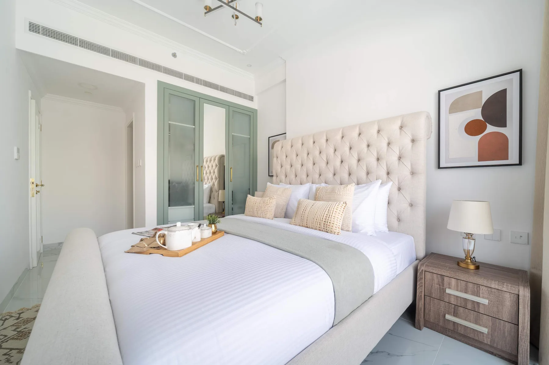 Un dormitorio luminoso con una cama bien tendida y una obra enmarcada sobre la mesita de noche.