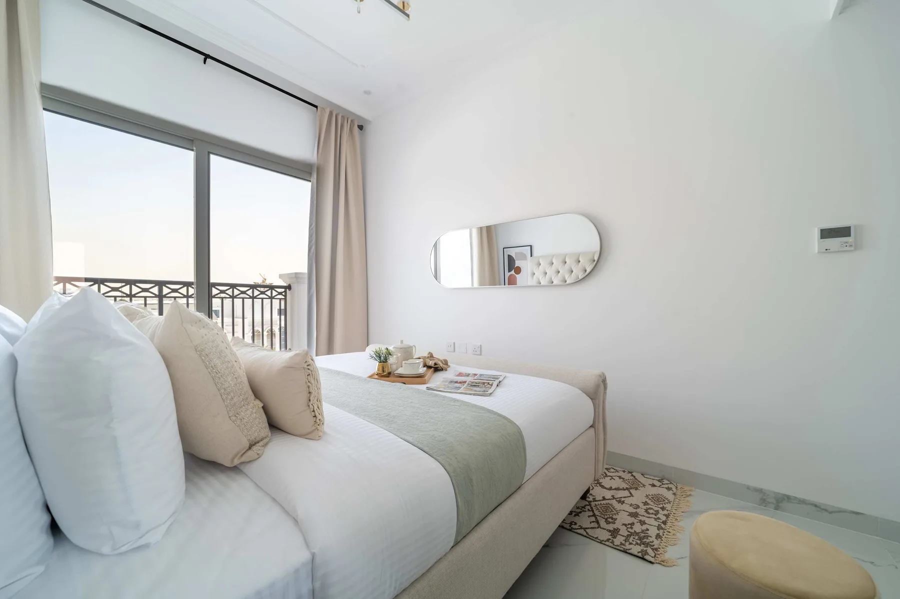 Dormitorio luminoso con una cama junto a ventanales y un balcón.