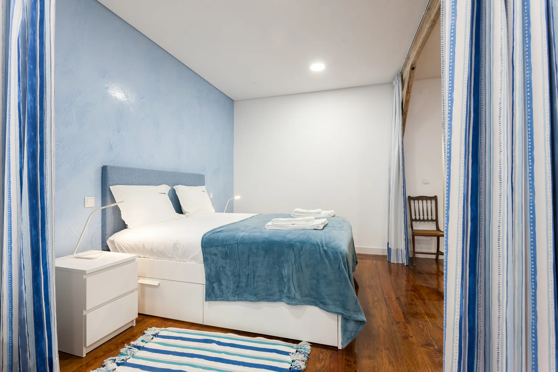 Un dormitorio con una cama vestida con sábanas blancas y una manta azul.