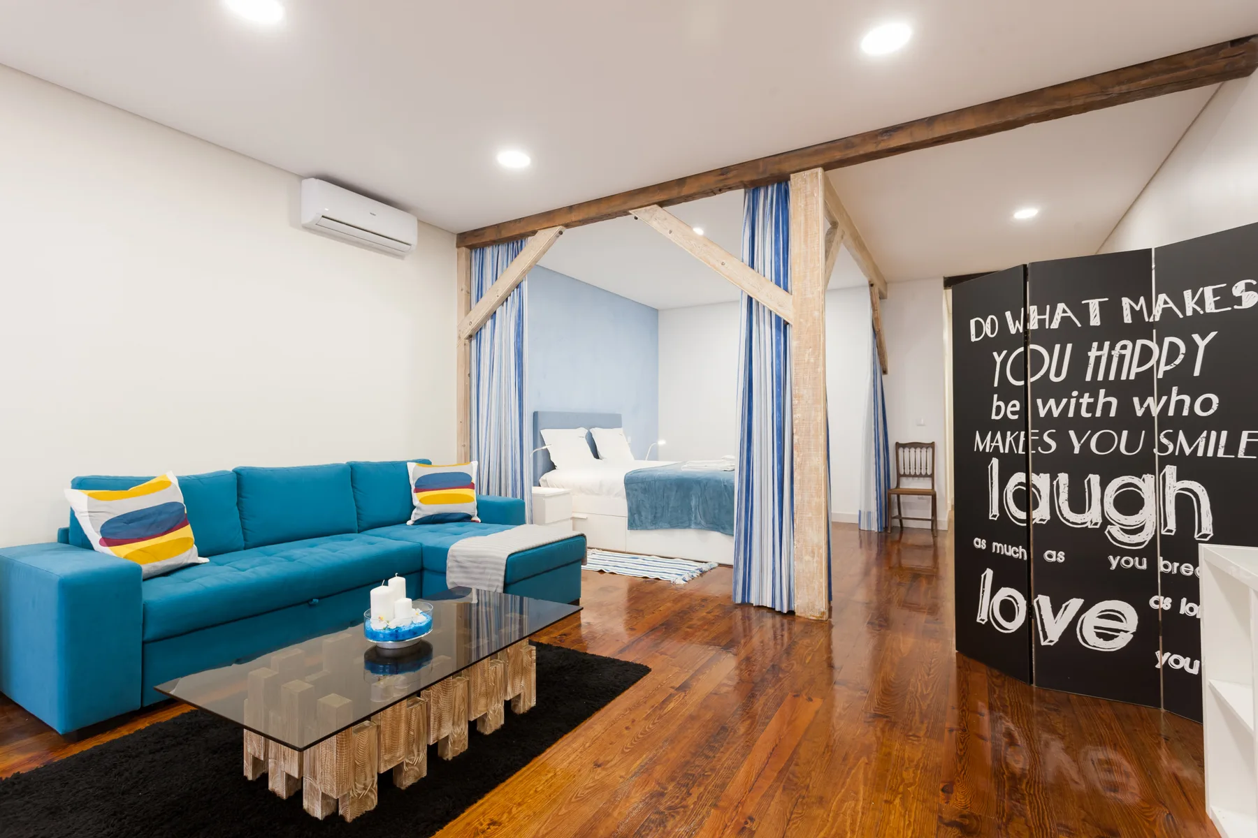 Una zona de estar tipo estudio con un sofá azul y una cama detrás de cortinas a rayas.