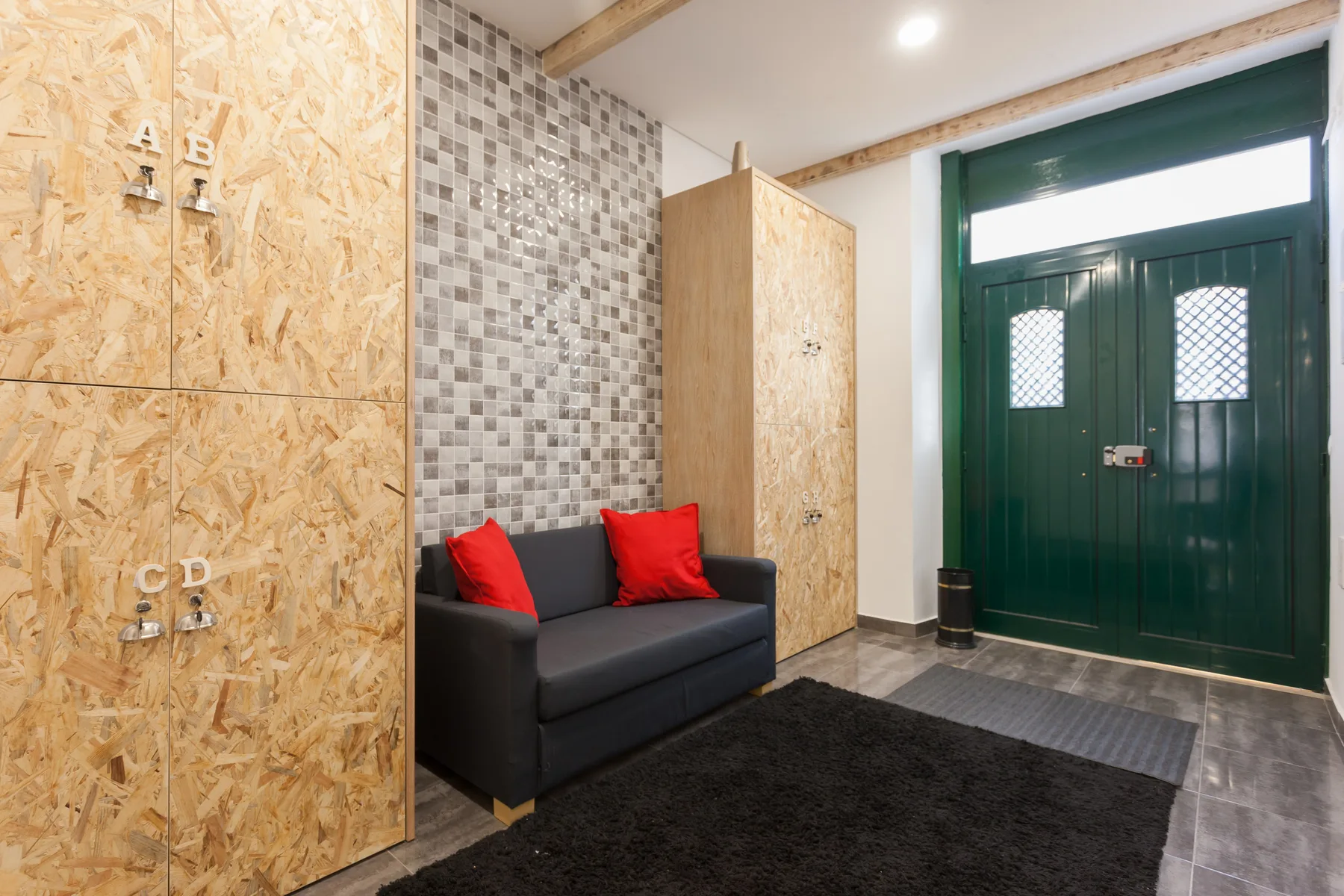 Una pequeña zona de estar con un sofá oscuro y cojines rojos junto a una puerta verde.