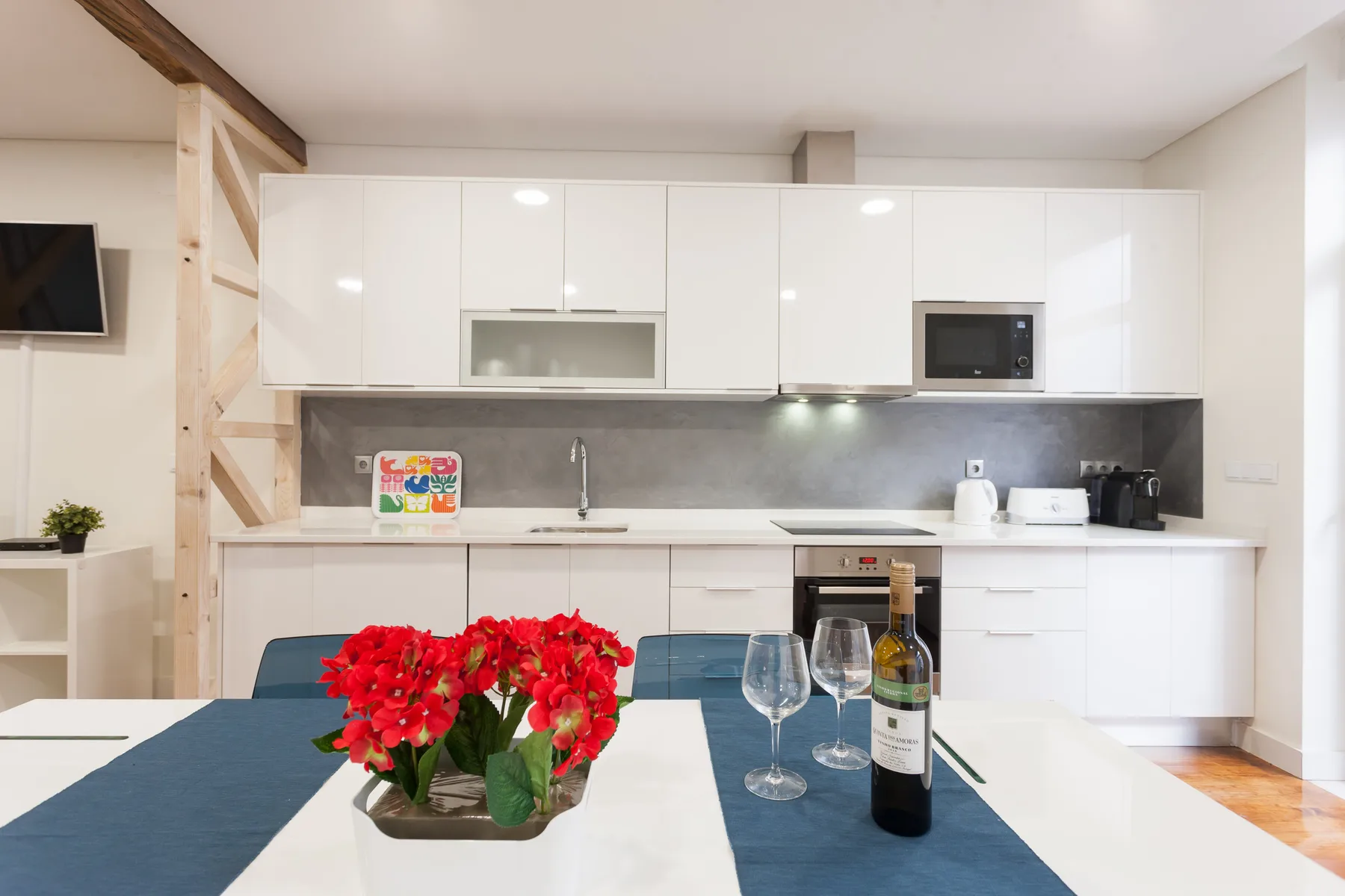 Una cocina luminosa con armarios blancos, una encimera y una mesa con flores.