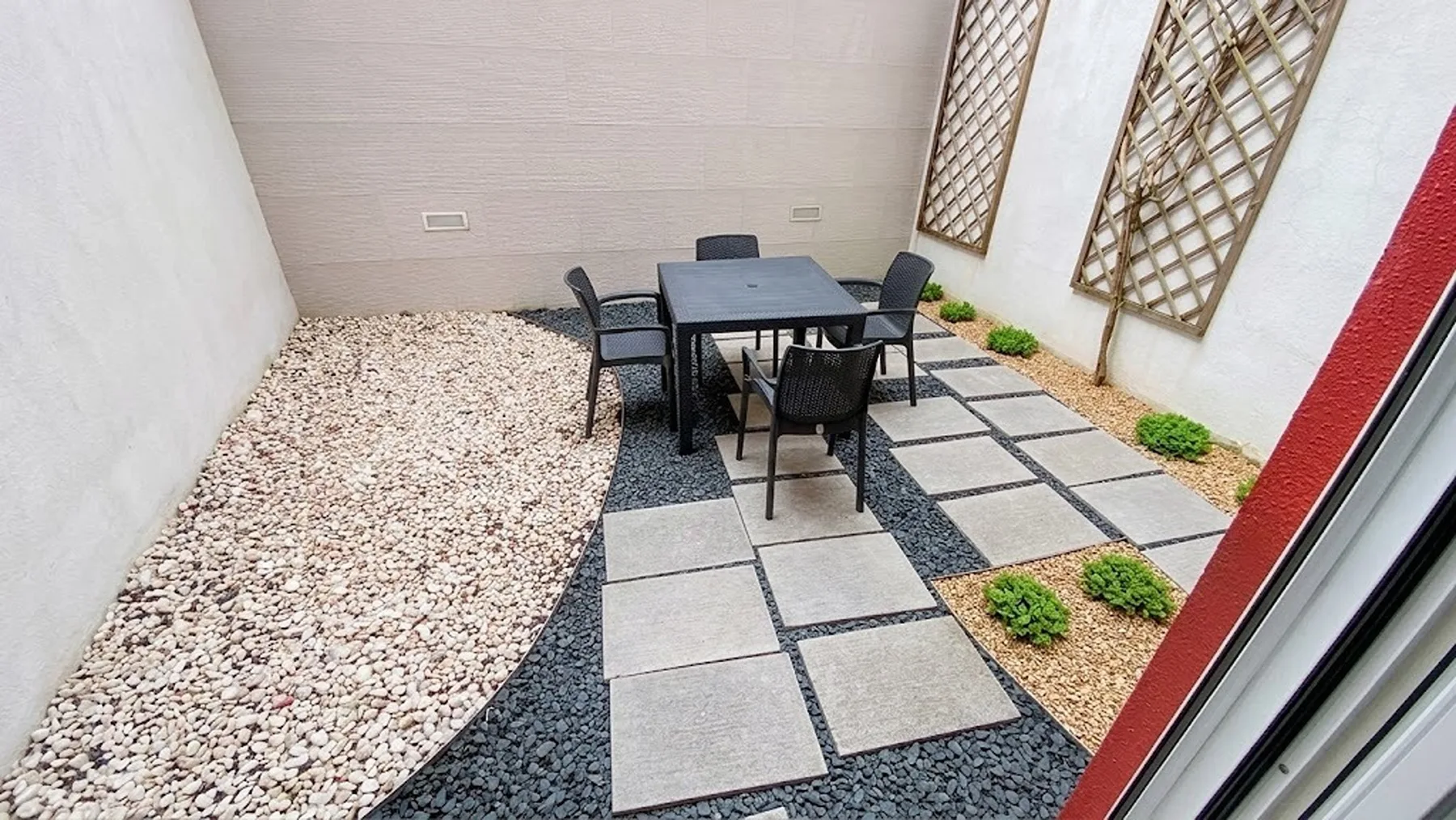 Un patio exterior con una mesa y sillas junto a un camino pavimentado.