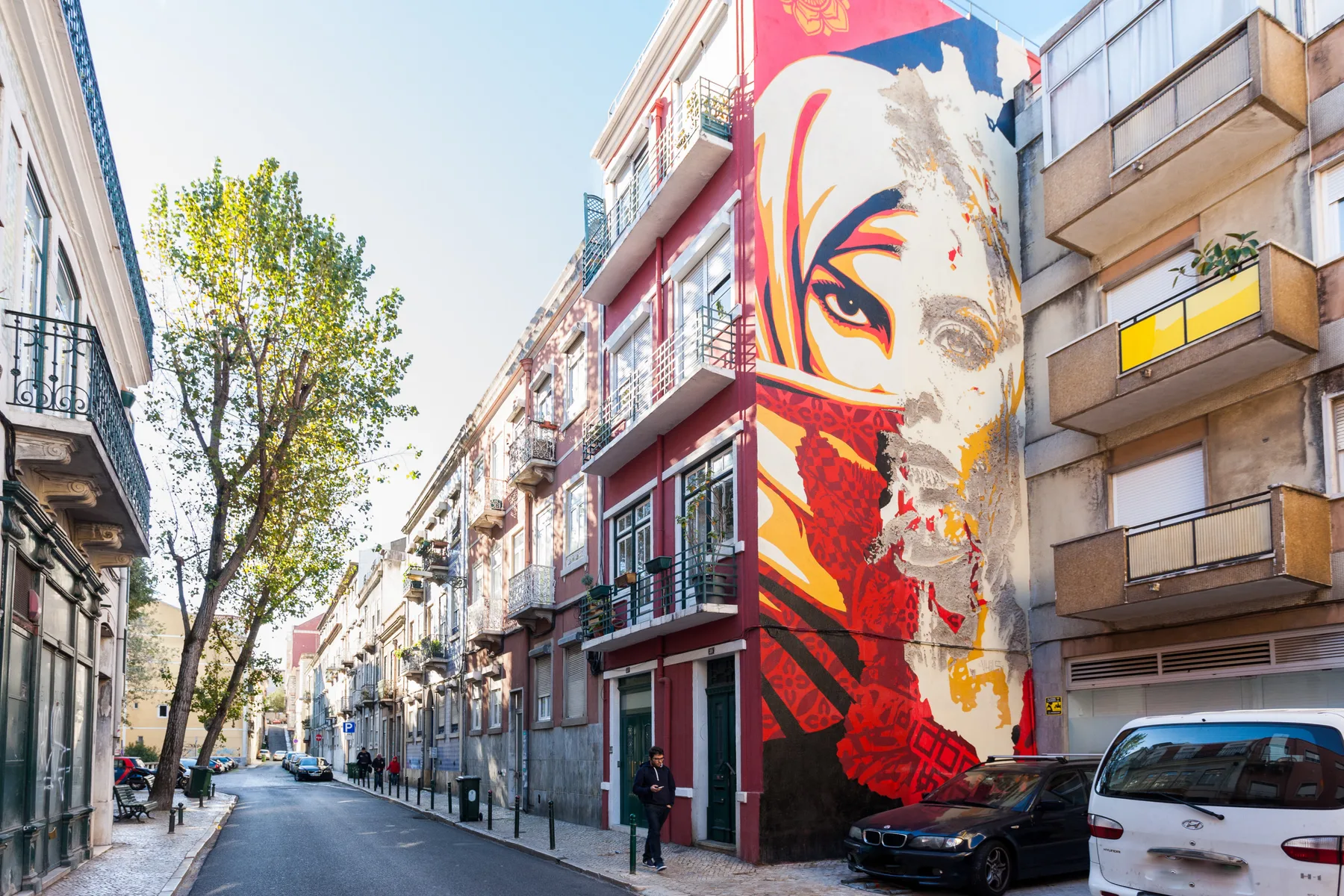 Una calle urbana bordeada de edificios de apartamentos, con un gran mural colorido.
