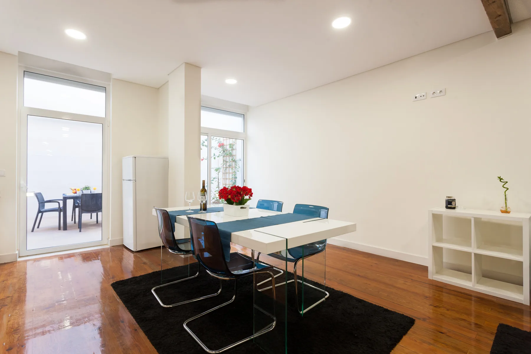 Una zona de comedor luminosa con una mesa y sillas junto a ventanas altas.