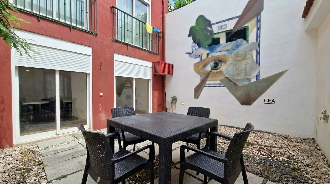 Un comedor en un patio con una mesa oscura, sillas y un mural.
