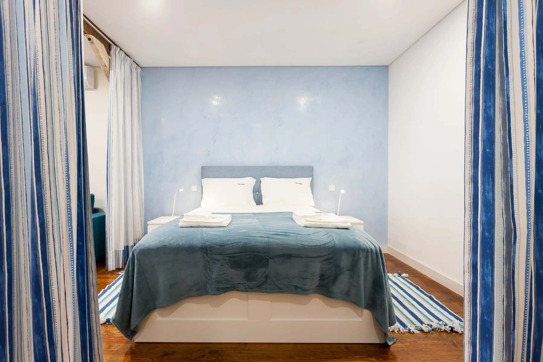 Un dormitorio con una cama vestida de azul y cortinas a rayas.