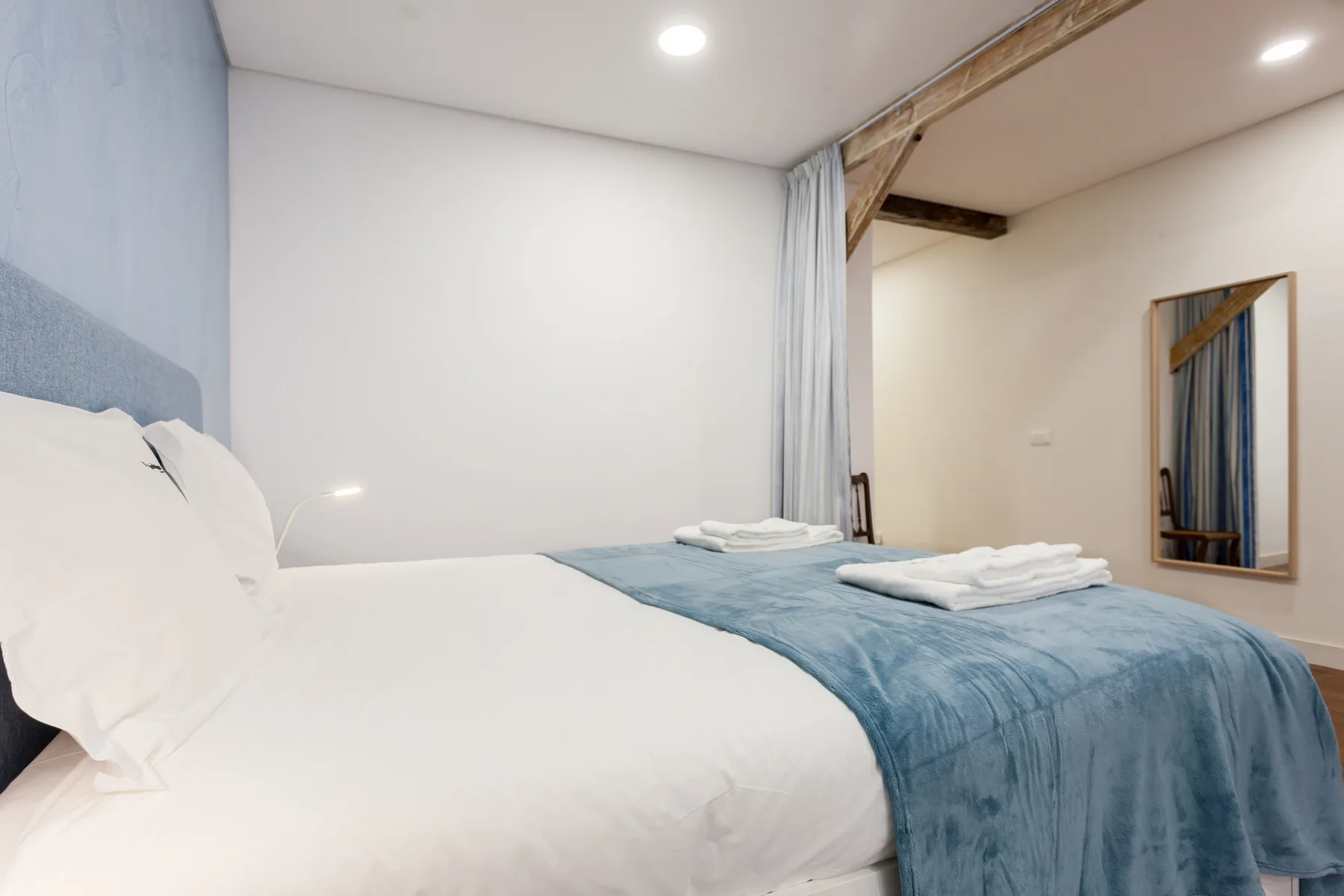 A bedroom with a bed dressed in white linens and a blue blanket.