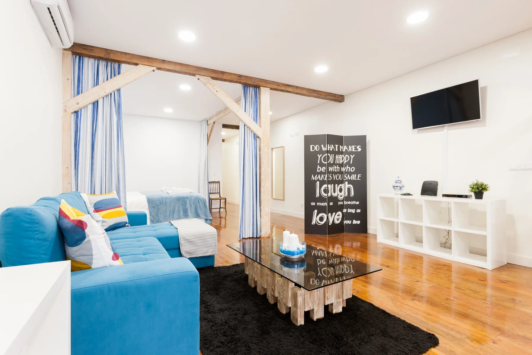 Una luminosa zona de estar tipo estudio con asientos azules, una mesa de centro de vidrio y un televisor en la pared.