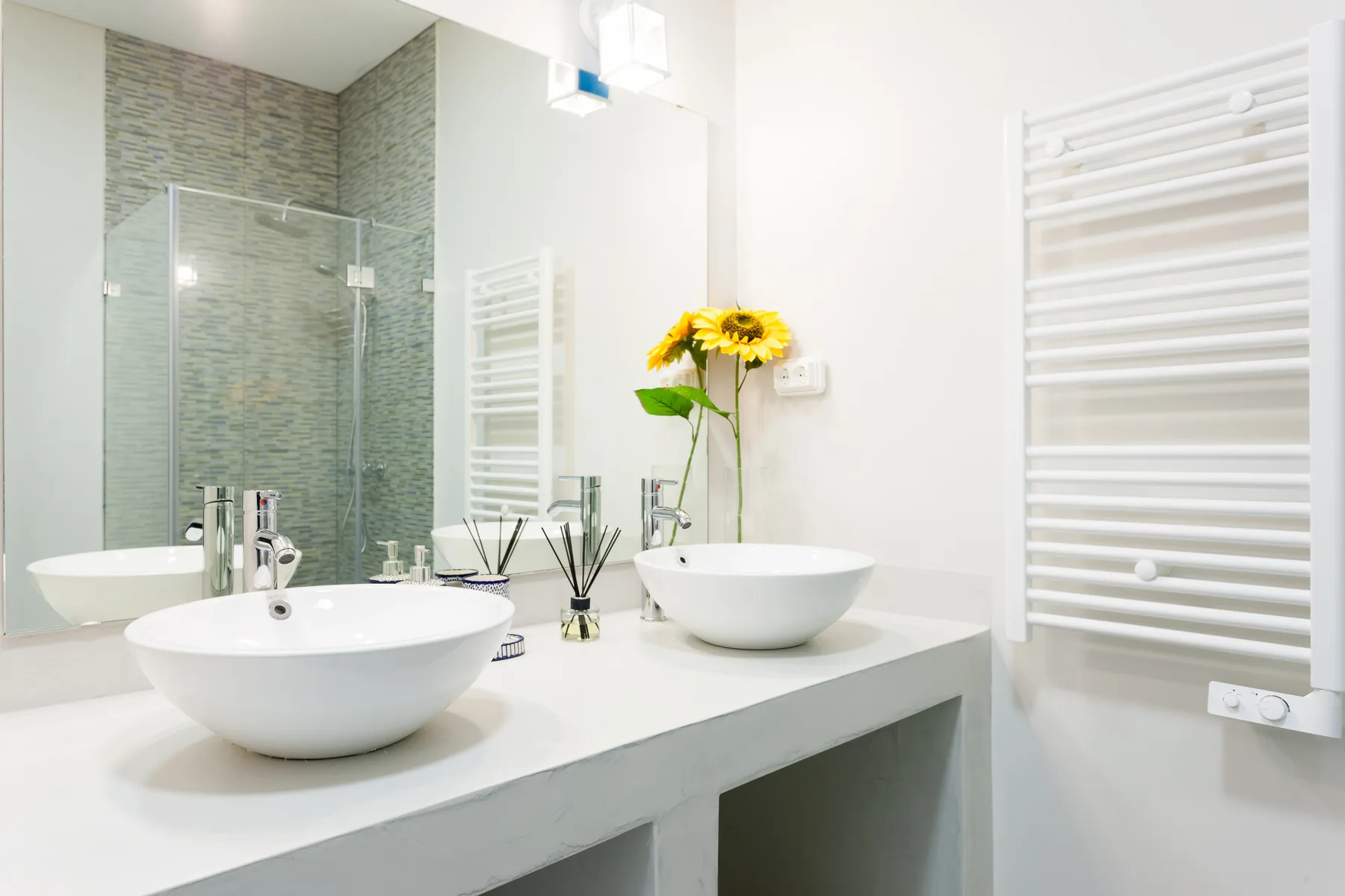Un baño luminoso con lavabos blancos sobre la encimera y una ducha de vidrio.
