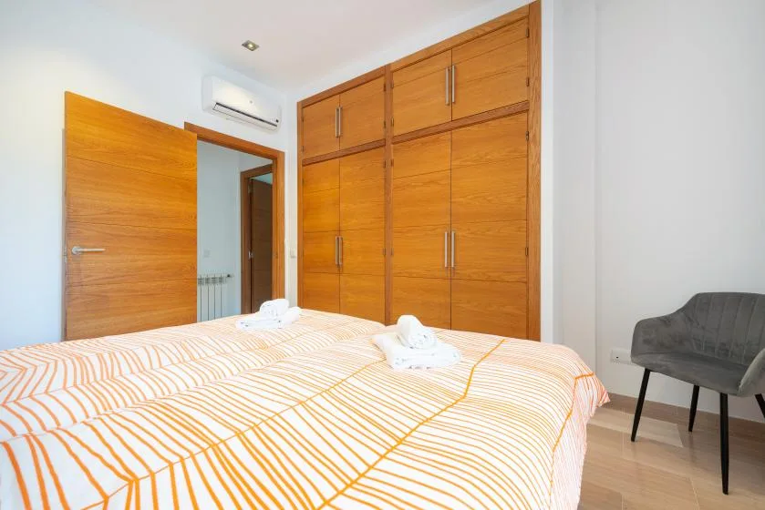 Un dormitorio con una colcha a rayas, un armario de madera y una silla gris.