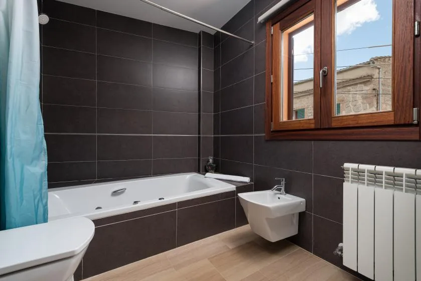 Un baño alicatado con bañera, bidé y ventana con marco de madera.