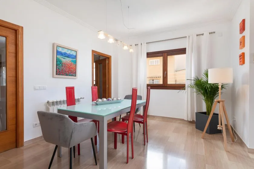 Un comedor con una mesa de vidrio y sillas rojas junto a una ventana.