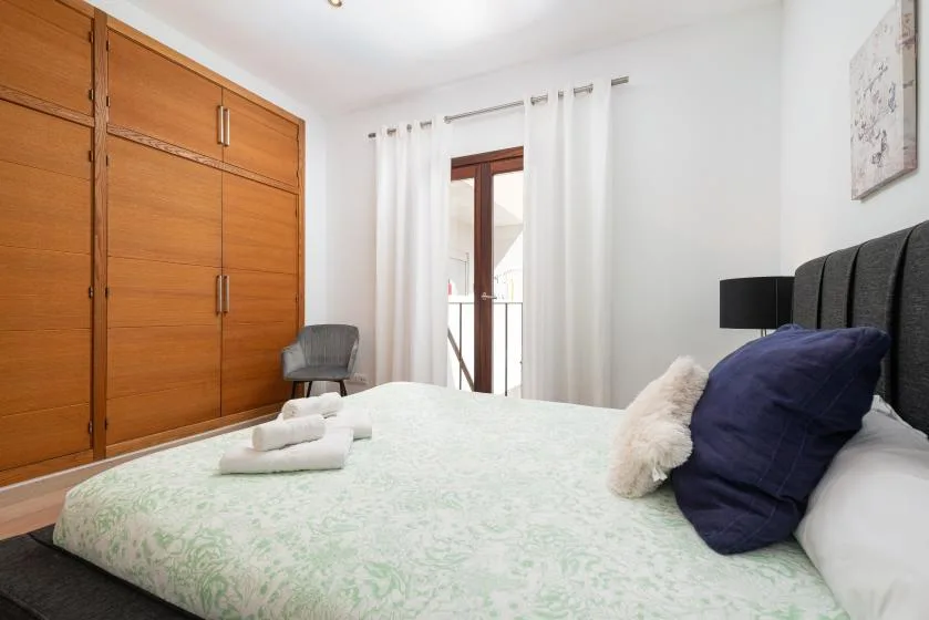 Un dormitorio con una cama, armarios de madera y una puerta acristalada con cortinas.