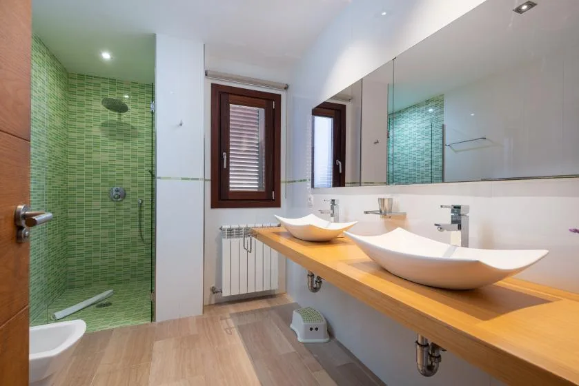 Baño con ducha de vidrio, una encimera larga y dos lavabos sobrepuestos.