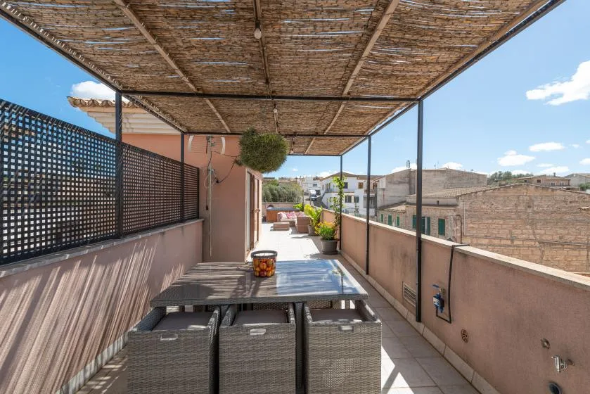 Una terraza exterior cubierta con una mesa y asientos bajo un toldo tejido.