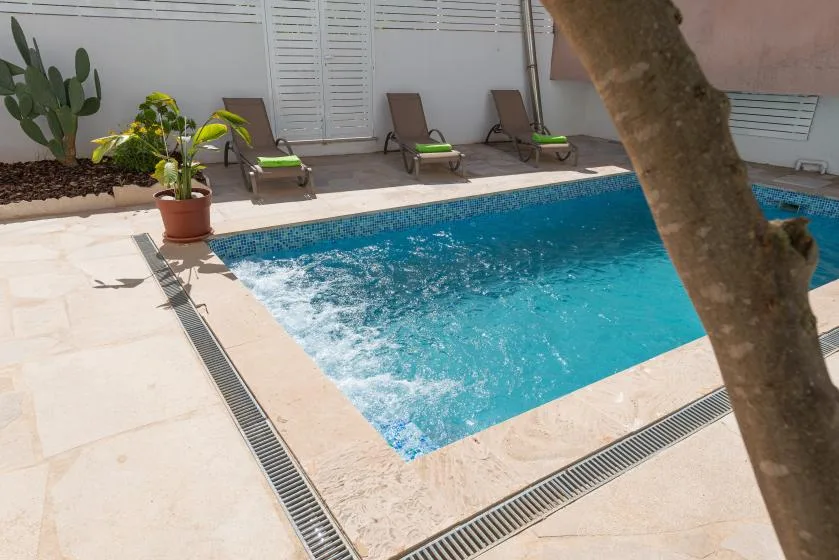 Una piscina junto a un patio pavimentado con asientos reclinables y plantas en macetas.