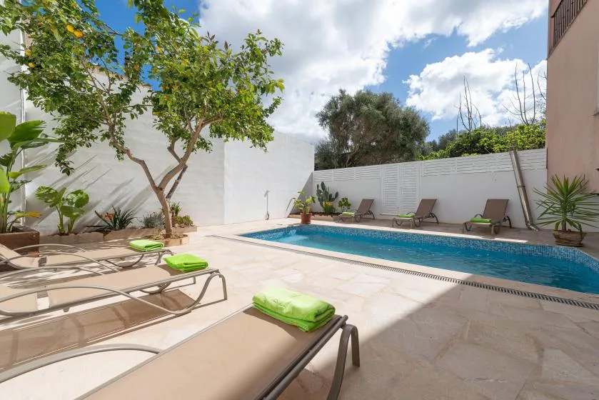 Una zona de piscina al aire libre con tumbonas y árboles junto a una pared blanca.