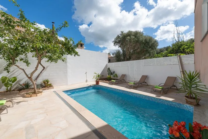 Una piscina al aire libre ocupa un patio soleado con sillas de descanso alrededor.