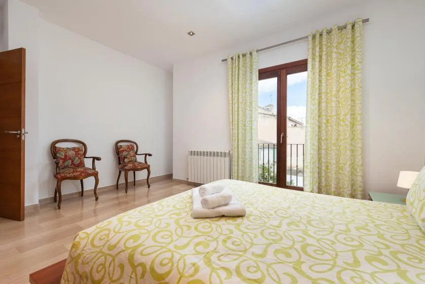 Dormitorio luminoso con una colcha estampada y una puerta acristalada que da a un balcón.