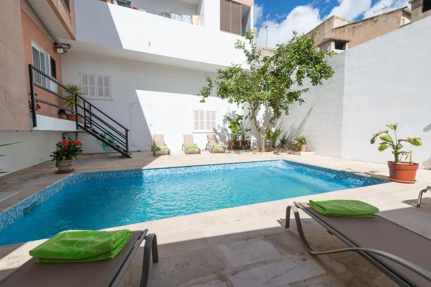 Una piscina al aire libre junto a un edificio blanco, con tumbonas cerca.