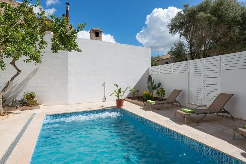Una piscina al aire libre junto a un patio de paredes blancas con asientos reclinables.