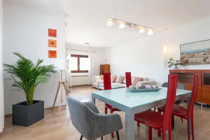 Una luminosa zona de comedor y estar cuenta con una mesa de vidrio y asientos rojos.