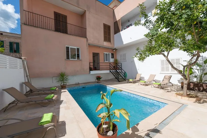 Una piscina en un patio está rodeada de asientos reclinables y un árbol frondoso.