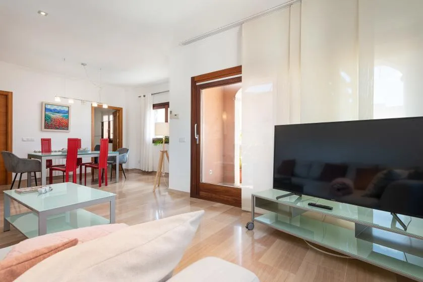 A bright living and dining area with a television and glass coffee table.