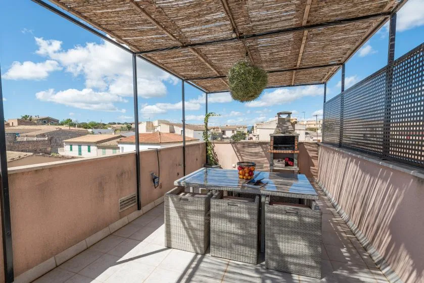 Una terraza comedor en la azotea con mesa, parrilla y toldo, con edificios cercanos a la vista.