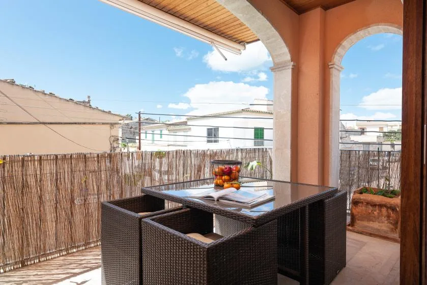 A covered balcony with a dark outdoor dining table and seating overlooks nearby buildings.