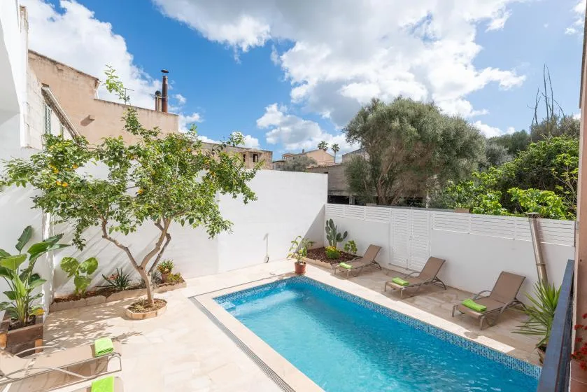 Una piscina al aire libre está en un patio pavimentado con asientos y árboles.