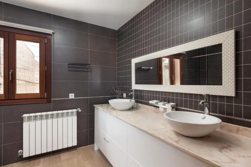 Un baño con azulejos, un tocador largo, dos lavabos y un espejo de pared.