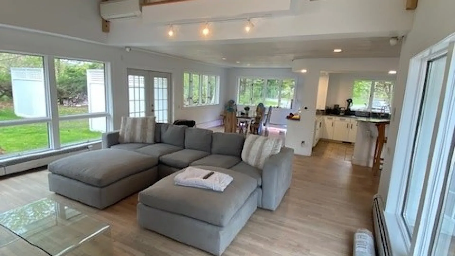 A bright living room with sectional seating and an open kitchen beyond.