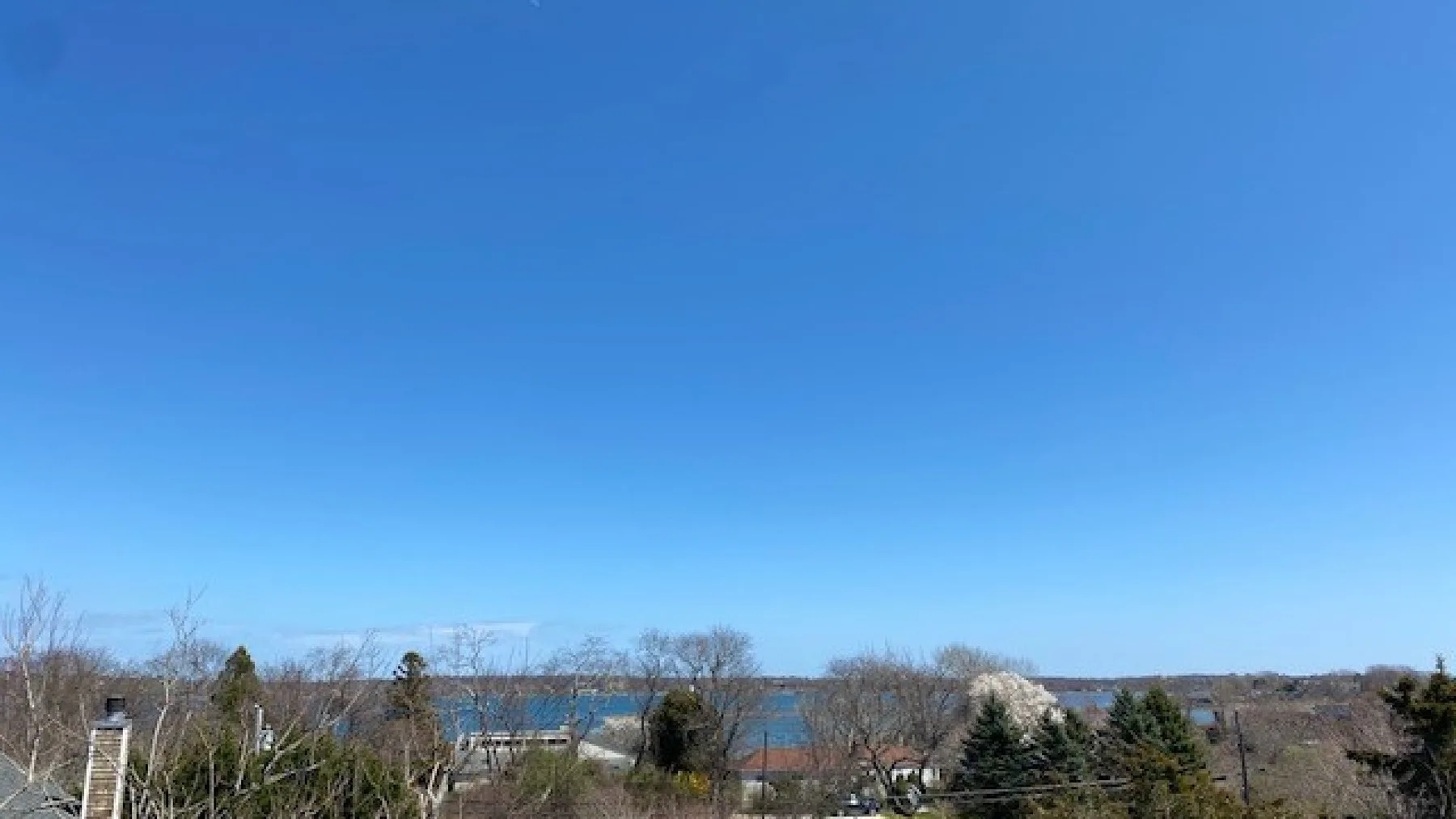 A broad outdoor landscape with trees, water, and a clear blue sky.