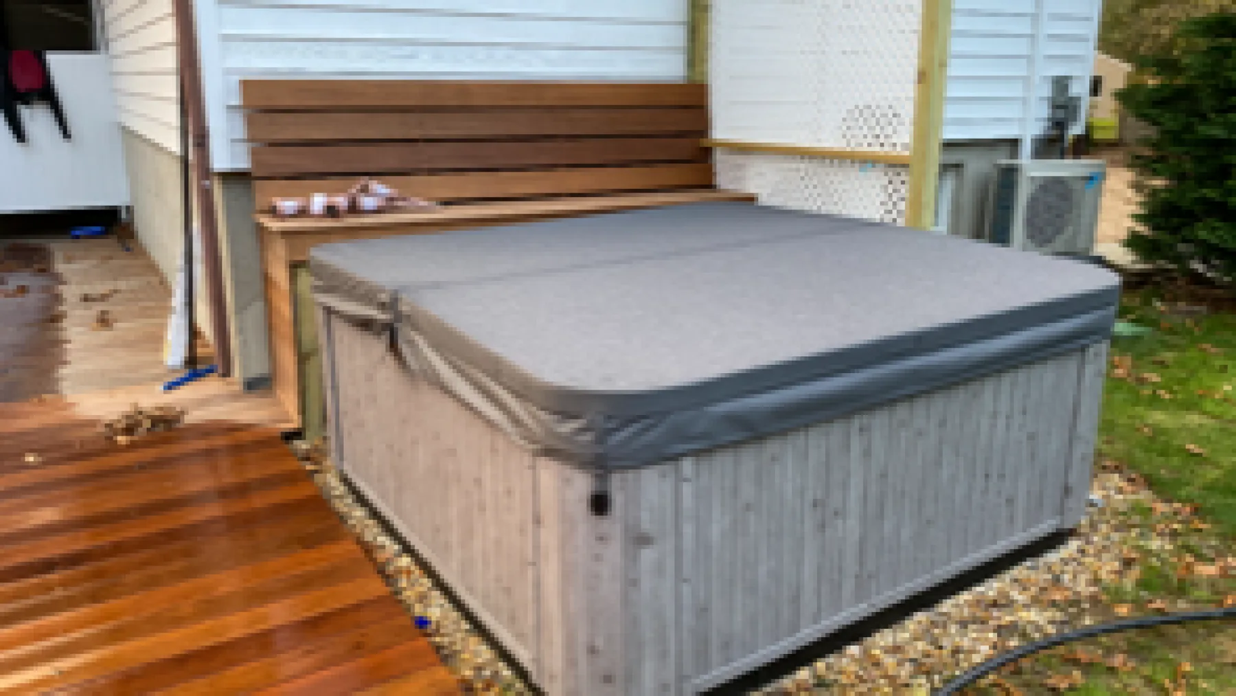 An outdoor hot tub sits beside a wooden deck and bench.
