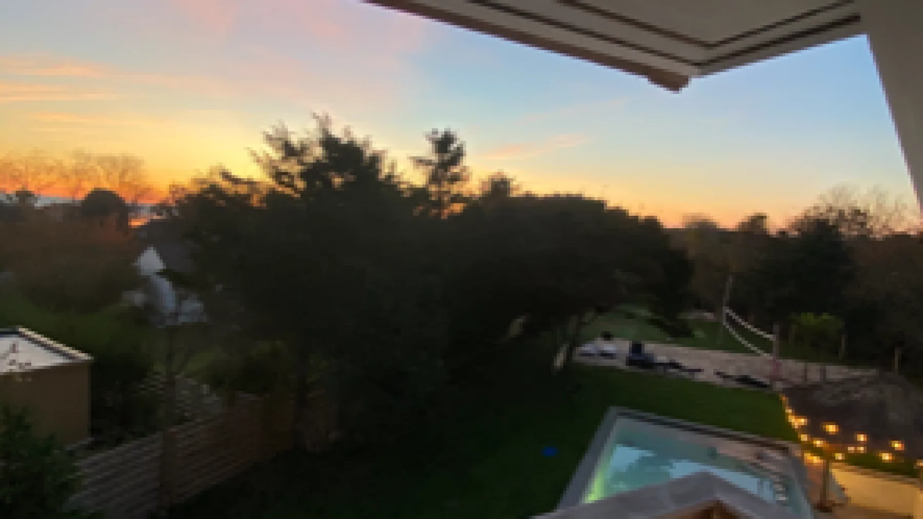 A backyard pool and garden are visible beneath a colorful sunset sky.