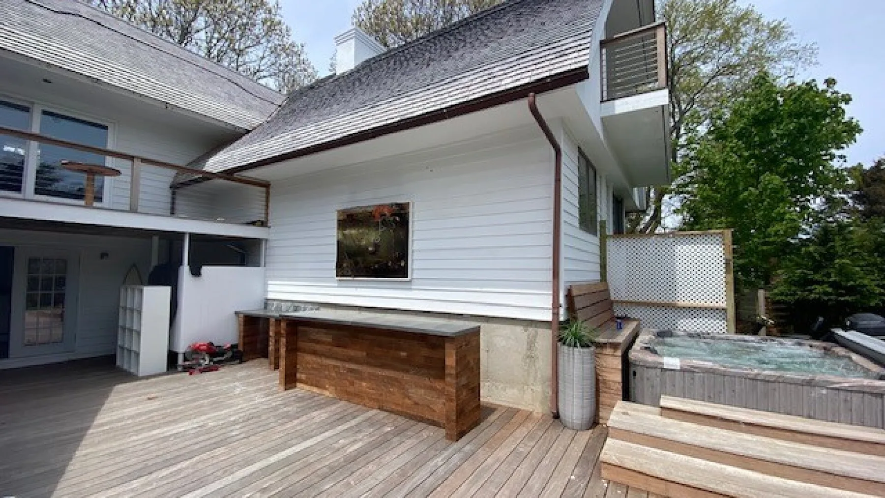 An outdoor deck beside a white-sided house, with a wooden counter and hot tub.