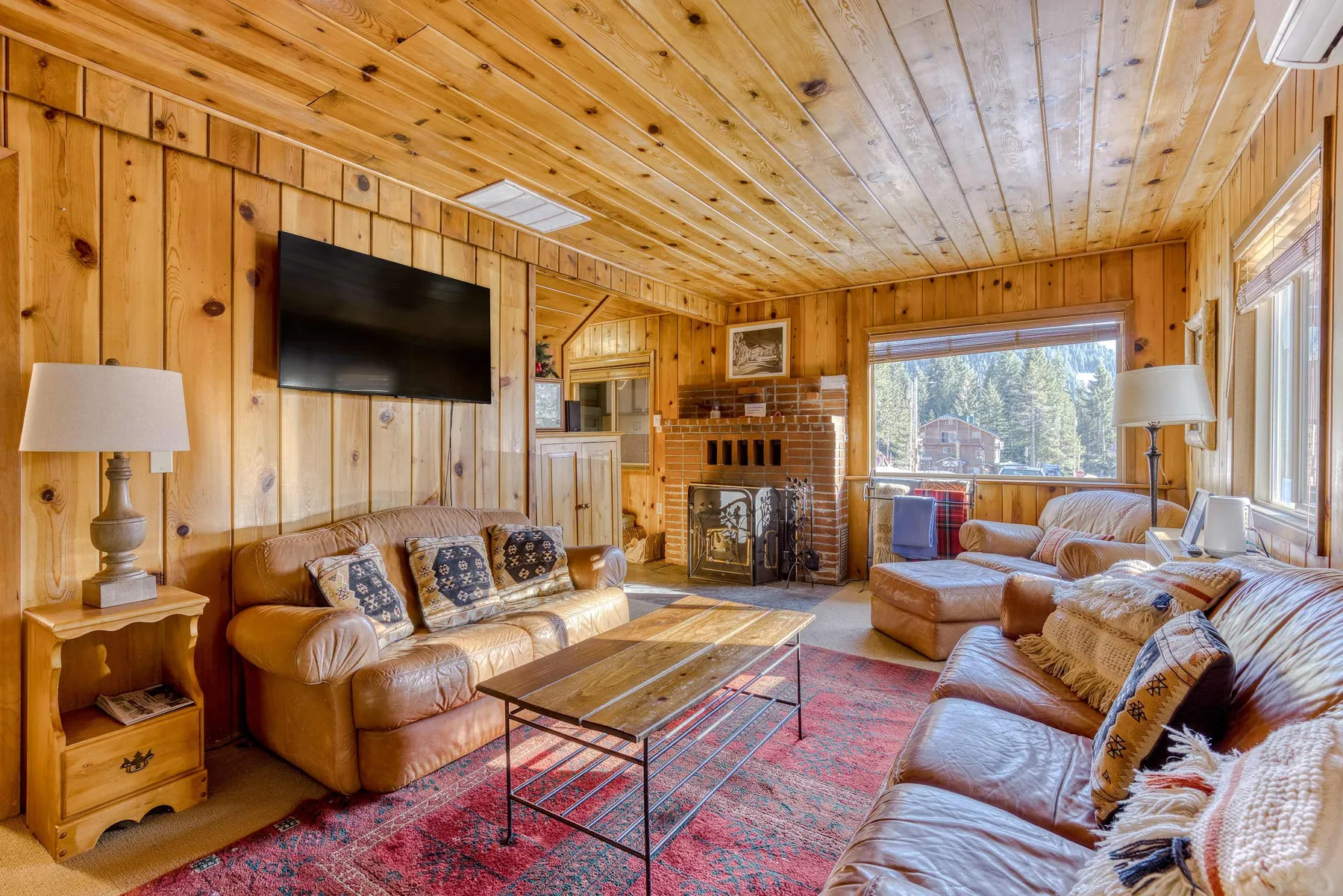 A wood-paneled living room with sofas, a fireplace, and a large window.