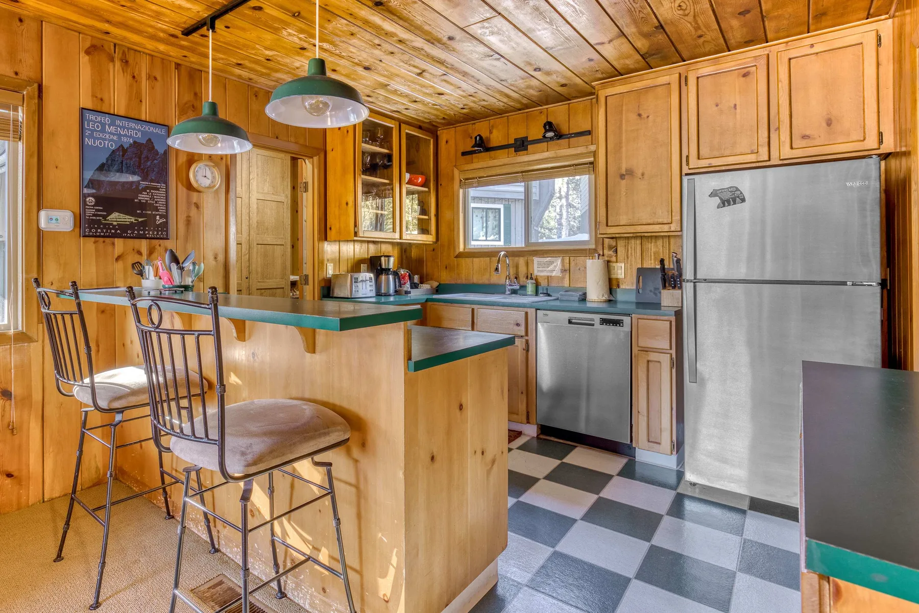 A wood-paneled kitchen with a counter, stools, and stainless steel appliances.