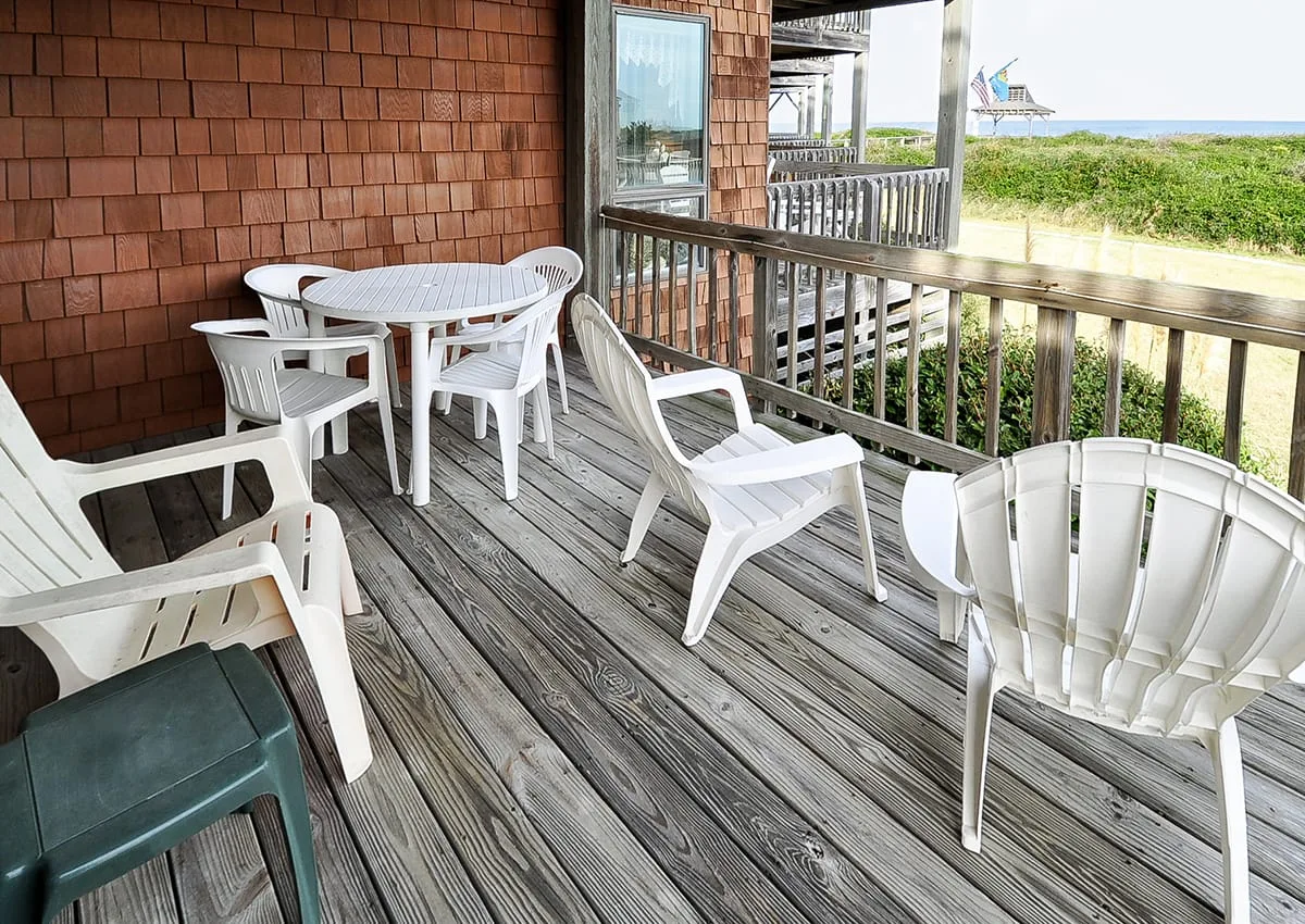 A wooden deck with white outdoor seating overlooks beach dunes and the ocean.