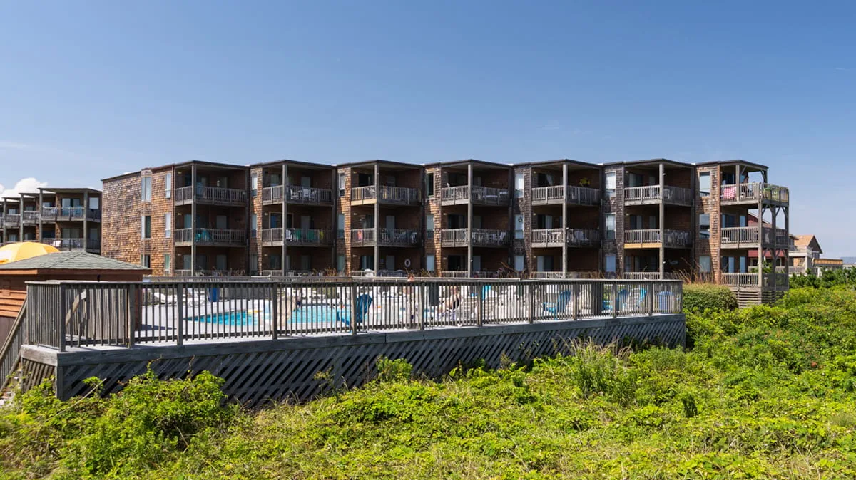 A multi-story building with balconies stands beyond a raised walkway and green landscaping.