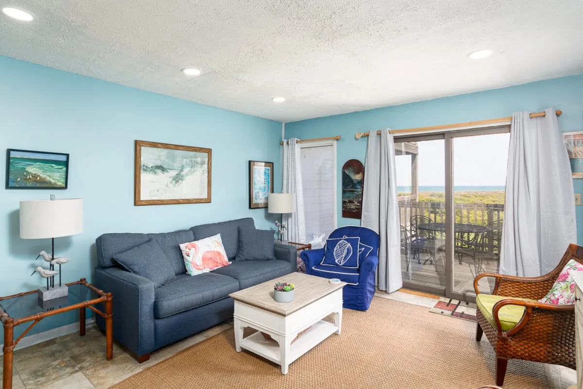 A bright living room with blue seating and a sliding glass door opening onto a balcony.