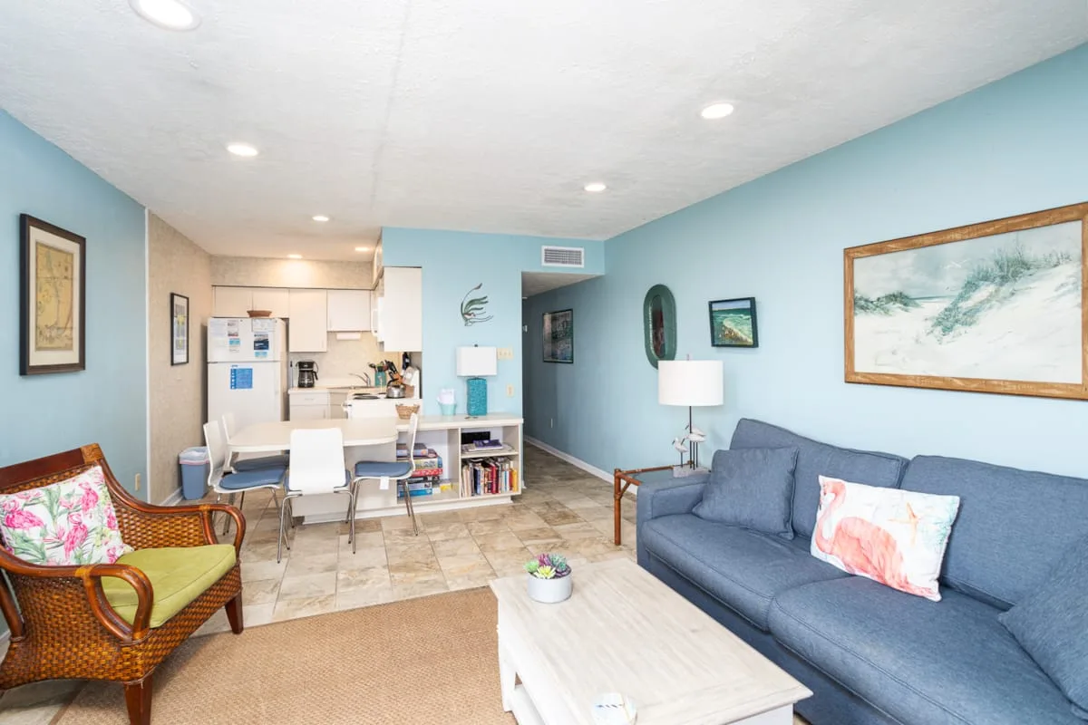 A living room with blue seating and a dining area beside the kitchen.