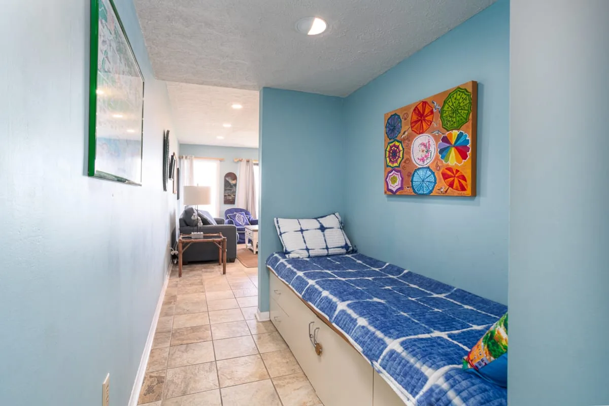 A narrow blue-walled sleeping area has a single bed and colorful wall art.