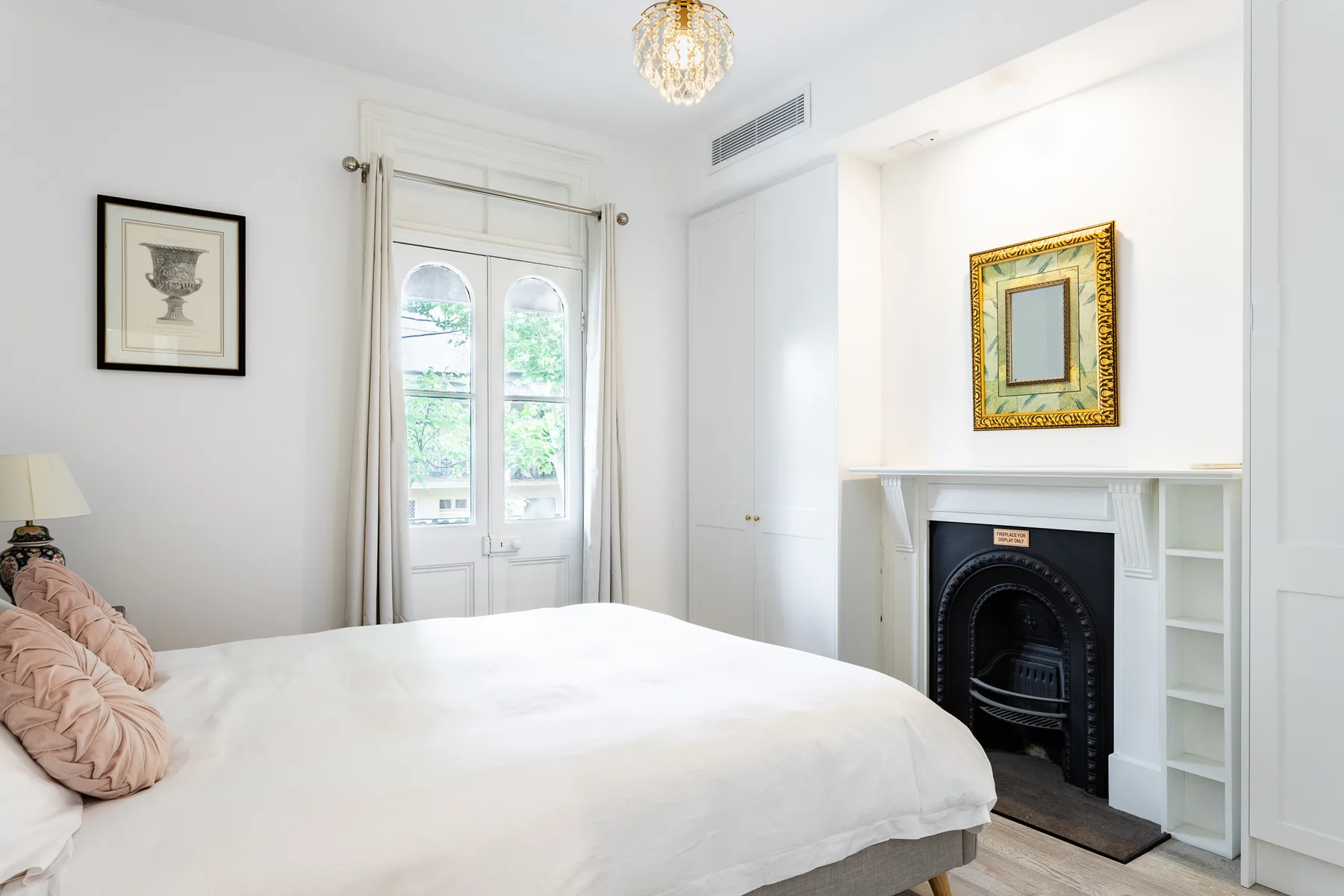A bright bedroom with a bed, tall windows, and a fireplace.