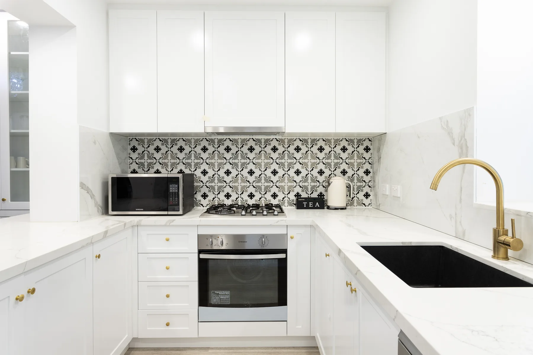 A bright white kitchen with a patterned backsplash and dark countertop.