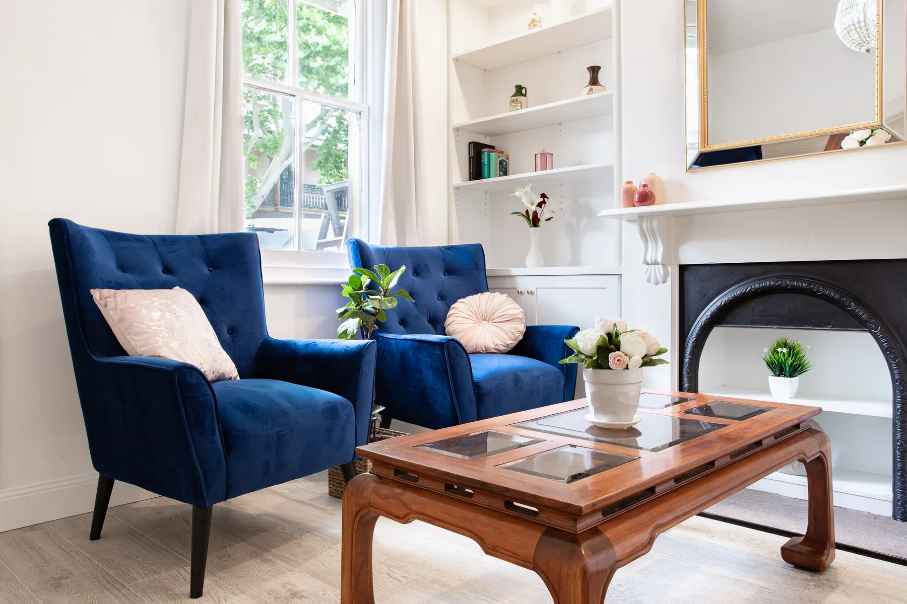 A bright sitting room with blue seating, a wooden coffee table, and a fireplace.