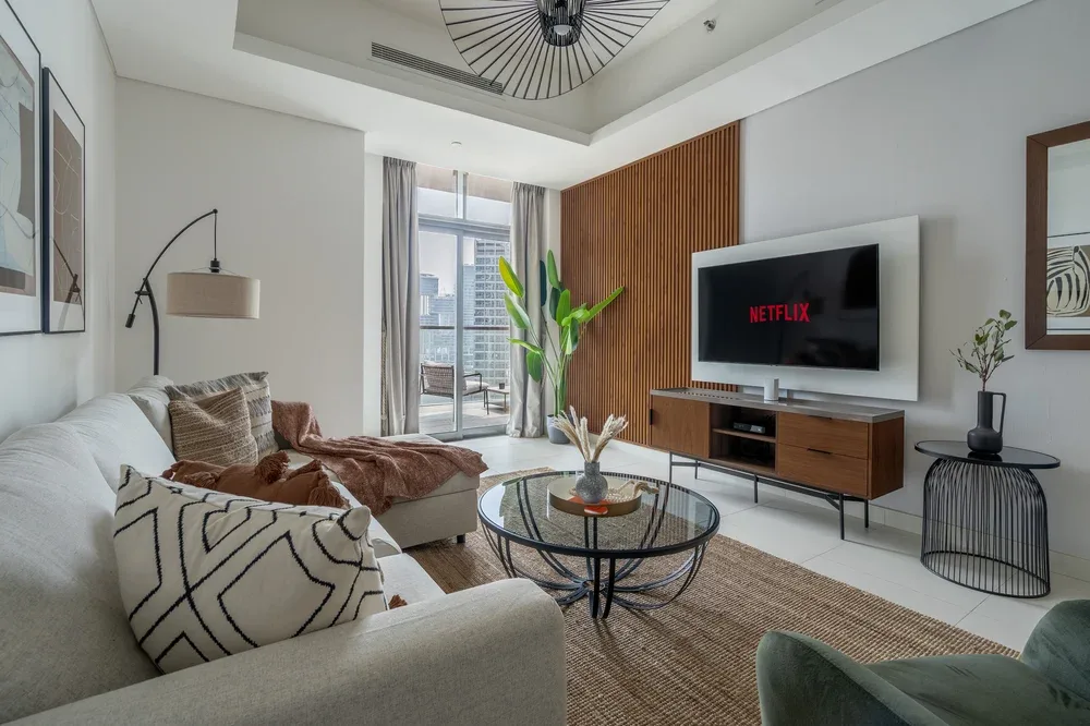 A bright living room with seating, a television, and a glass coffee table.