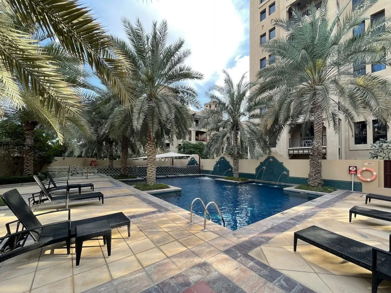Una piscina al aire libre está rodeada de palmeras y asientos para descansar.